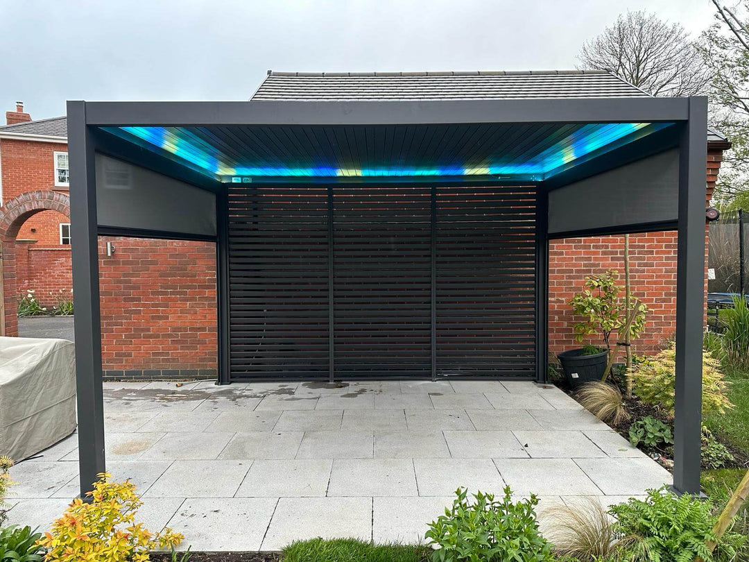 Titan Aluminium Pergola Anthracite Grey with Blue Lighting in new build house back garden against garage brick wall 