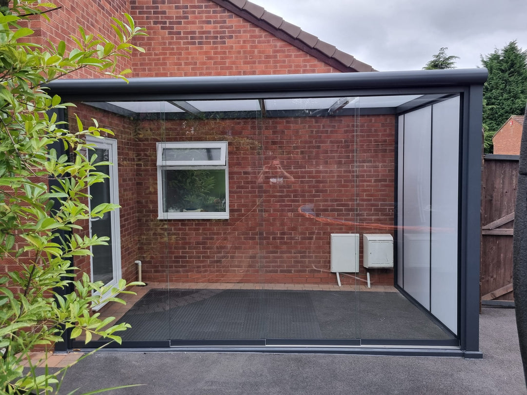 A Deponti Bosco veranda installed to the side of a bungalow house in anthracite grey colour with clear Fiano glazing to the front. 
