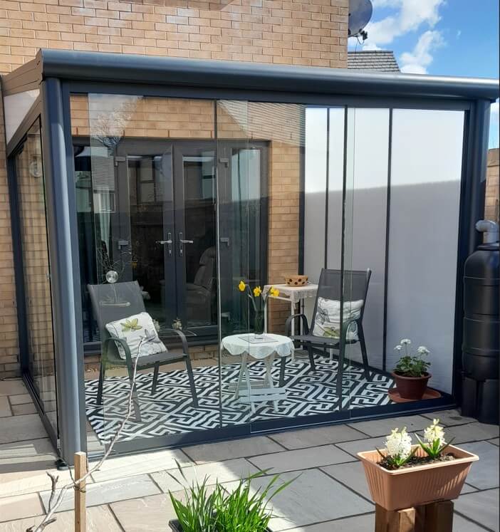 Modern DePonti Bosco Veranda Garden Room in Anthracite grey with Fiano Sliding Glass extension with glass doors and windows on a brick house exterior.