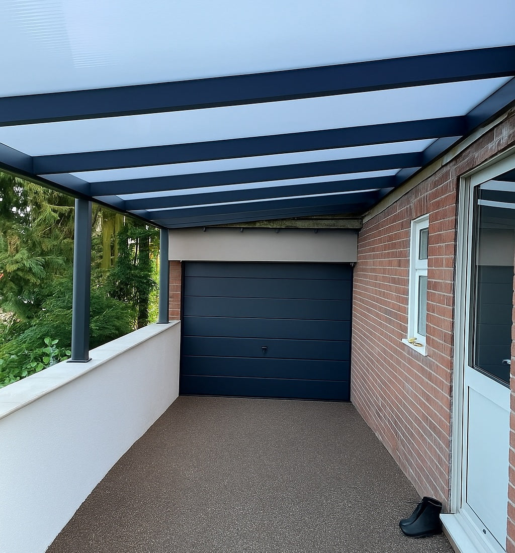DePonti Carport grey frame with opal frosted polycarbonate roof, against house with dark grey garage door and resin driveway.