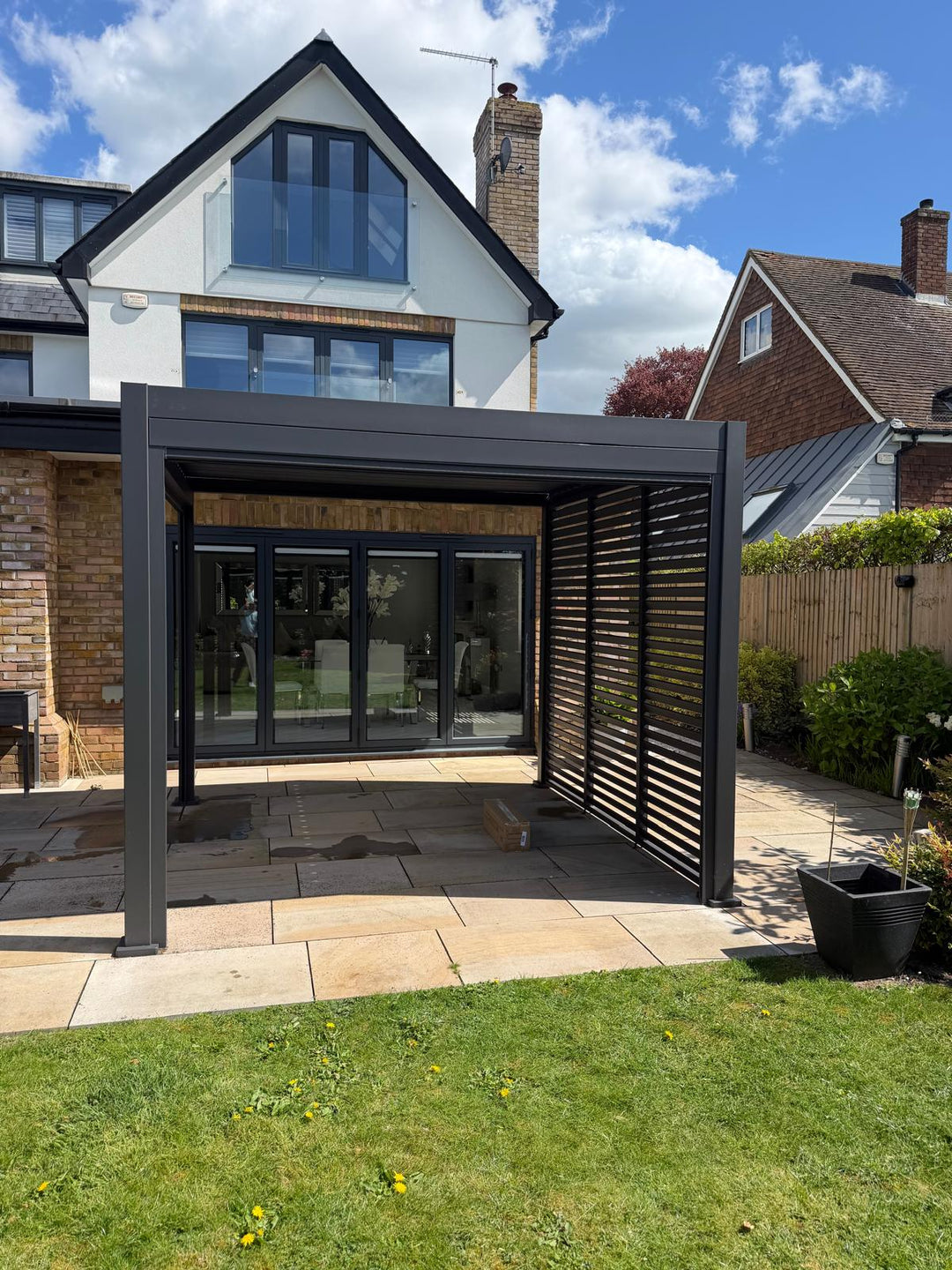Modern house with a Grey pergola in the garden. Nova Titan Aluminium Pergola Installation Leicester, Leicestershire by Midland Garden Furniture. In rear garden of beautiful large modern house on sunny day.