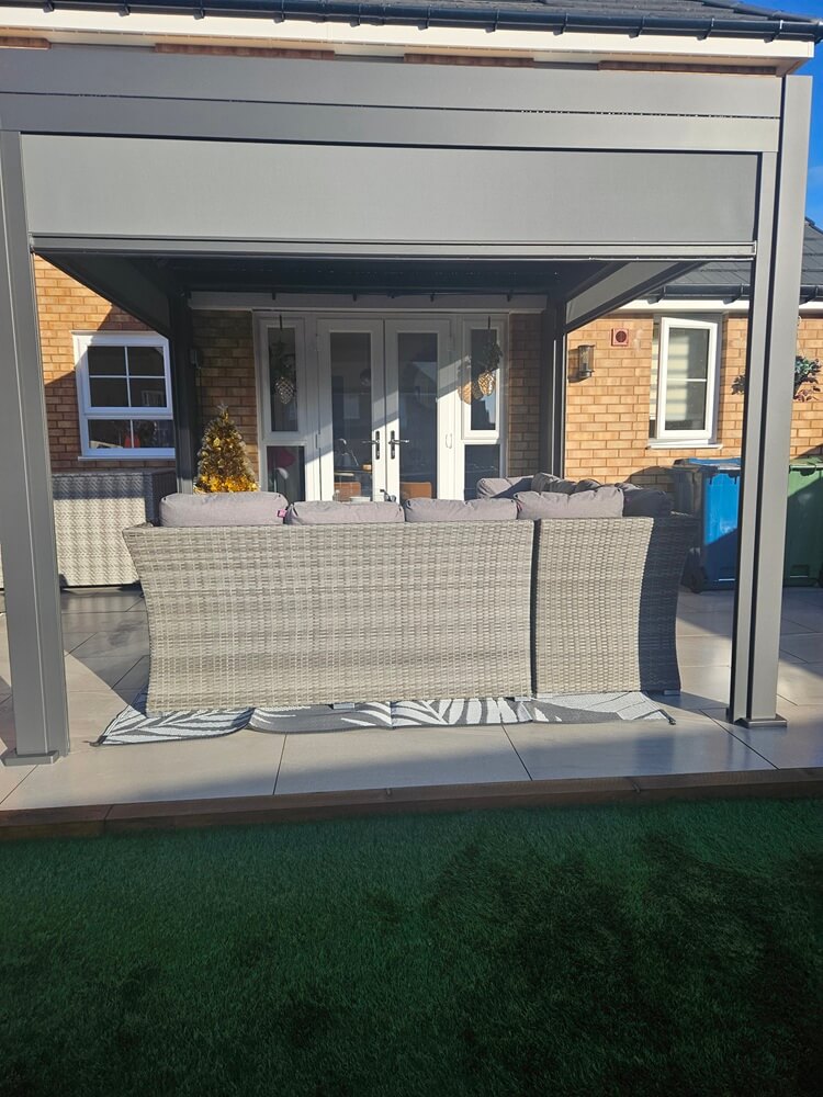 Grey Nova Titan pergola against new build home in back garden, with new light grey rattan garden furniture on porcelain tiles.
