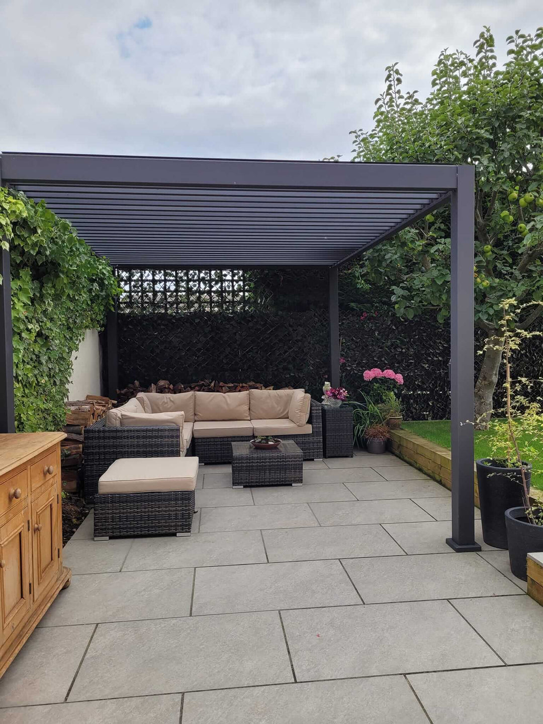 Grey Pergola on a new porcelain tiled patio area with cream garden sofa under and plants to the side