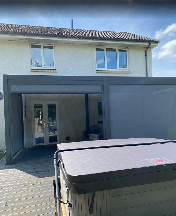 Hot tub on a decking area in front of a cream house with an Aluminium Pergola grey 6M x 3M with privacy screens for shade..