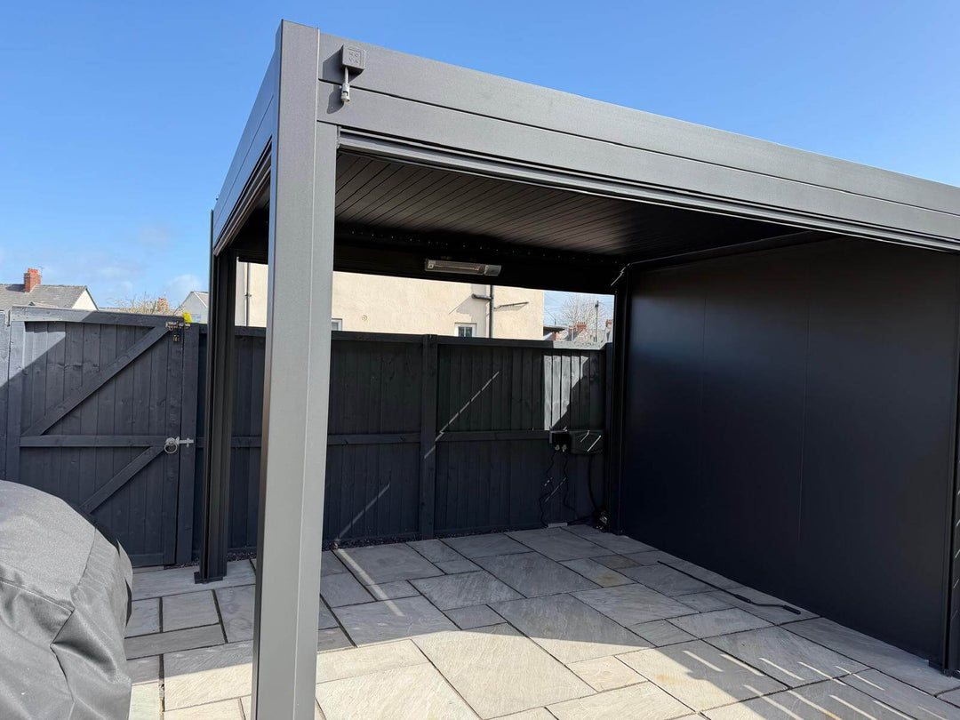 Nova Titan Pergola installation in Sherborne Dorset with New Nova Solid insulated aluminum walls with grey fence behind and wooden fence behind on slabbed patio area. Bright blue sky behind.