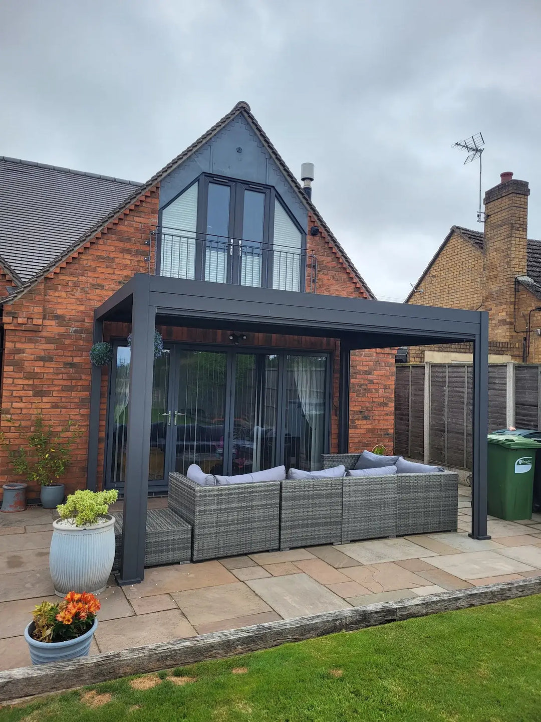 Grey Titan Pergola in back garden against brick house with large windows
