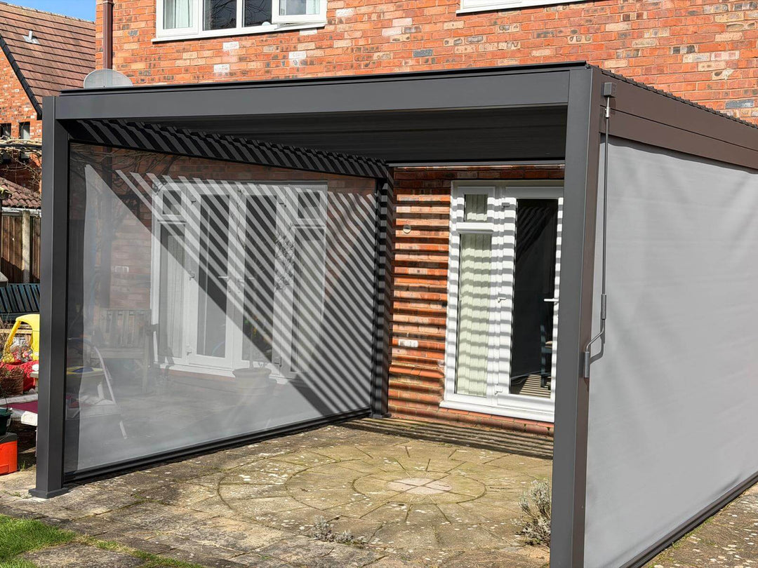 Nova Titan Aluminium Pergola in Anthracite grey installed on sand stone slabs with a large brick house behind with white windows and patio doors. Installed in Preston Lancashire. With children's playhouse behind.