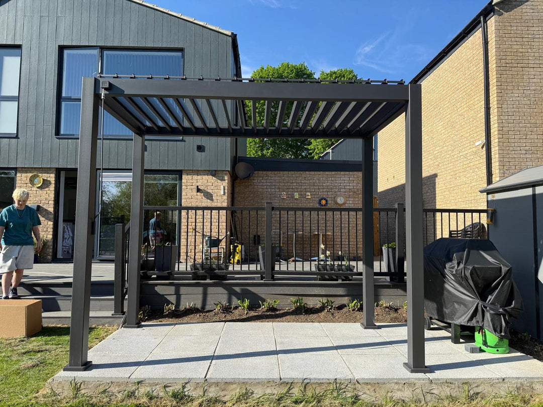 Grey Titan Pergola on bright white slabs in front of modern house with glass windows and blue sky 