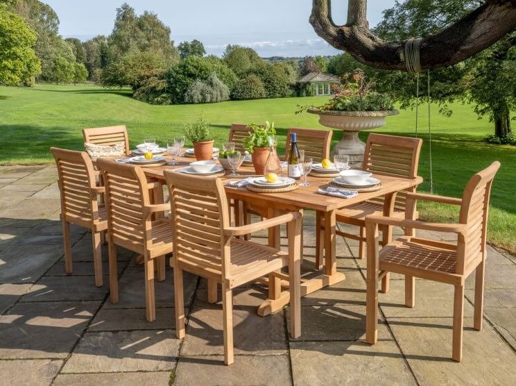 Hanover Teak Dining Set with rectangular table and 8 teak chairs on patio area with huge garden behind in manor house.