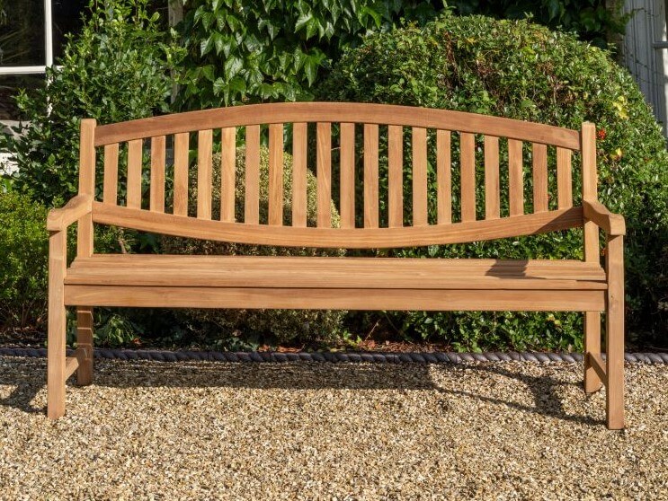 Hanover Teak Wooden bench in a garden setting with greenery in the background
