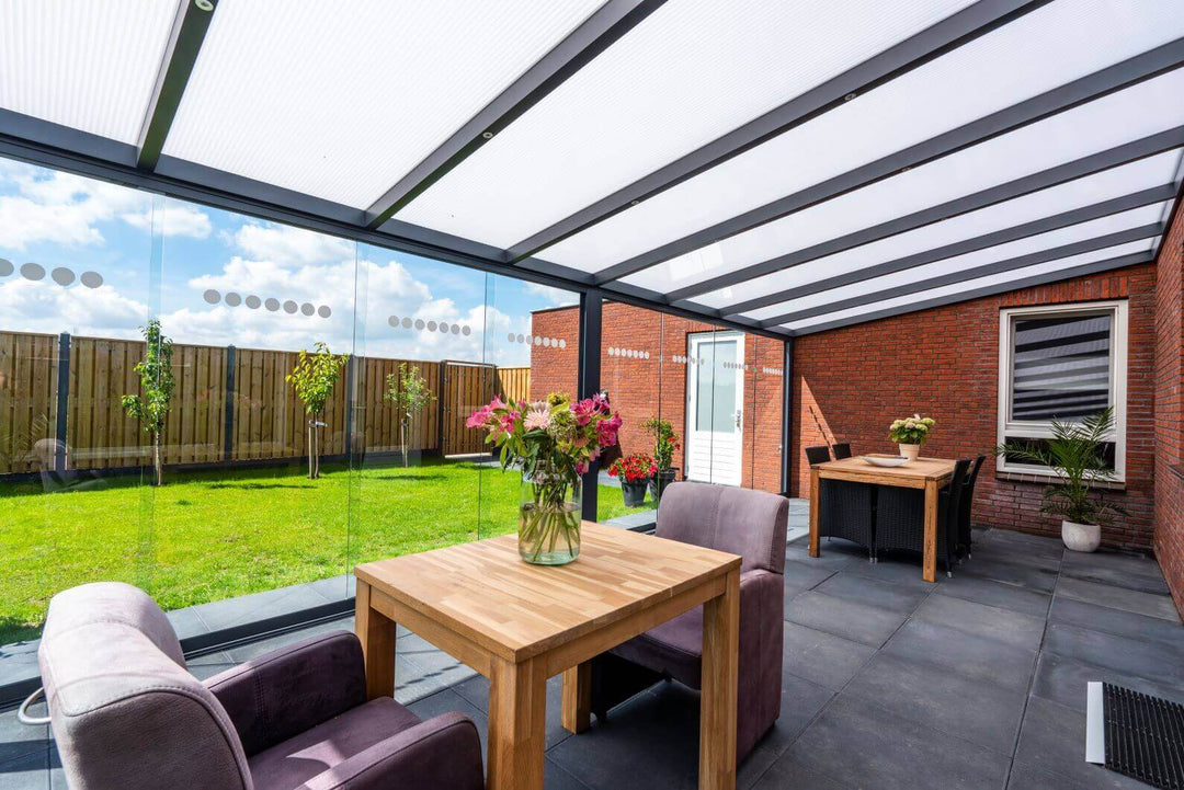 Large Bosco Veranda with frosted opal roof, and Fiano glazing to the from. dark grey tiles with two arm chairs and a table and dining table. 