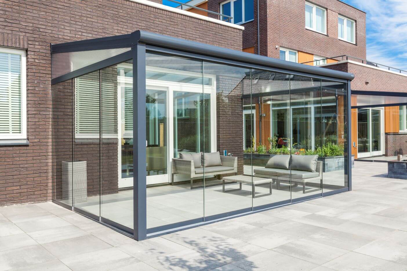Deponti Bosco Grey Veranda with Fiano sliding glazing on very modern light grey tiles on back of house with light grey rattan furniture inside.