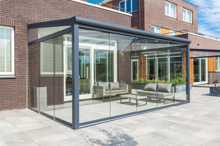 A modern Deponti BOSCO aluminium veranda with a polycarbonate roof, installed beside a residential building, providing a covered outdoor space.