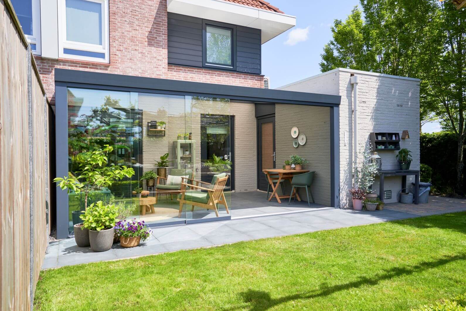 DePonti Pigato Bosco Garden room at the rear of a house between 2 walls. Modern sliding glazing to front, with light grey slabs inside and out and green garden furniture.