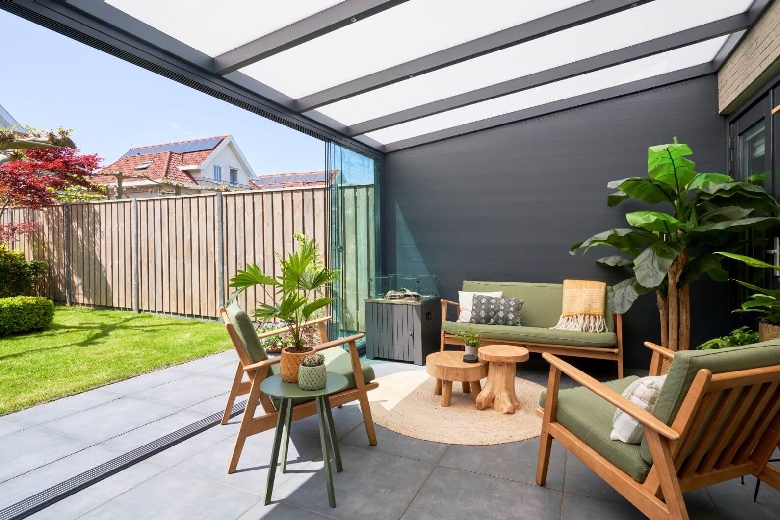 Inside view of DePonti veranda garden room, dark grey frame and solid wall, Fiano glazing to left to garden and green outdoor garden furniture.