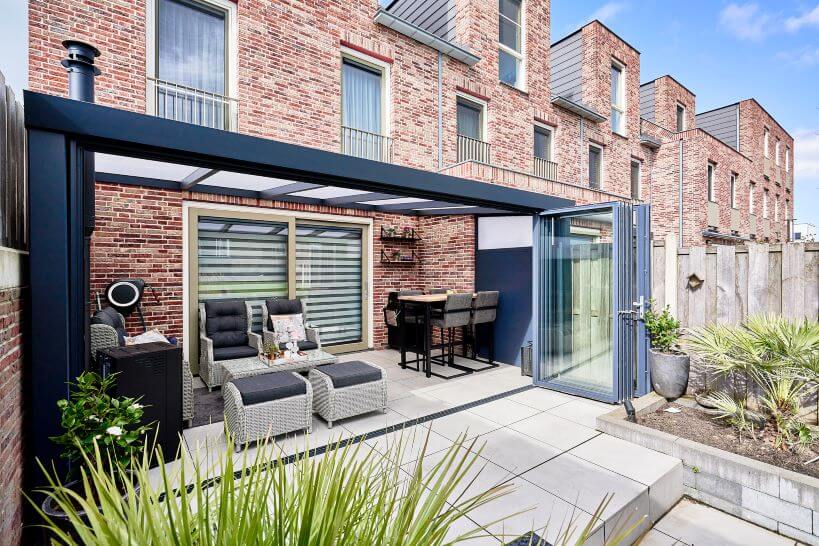 Deponti Veranda to the rear of a modern house. Fiano glazing to the front and opal roof. modern slabs and tall grass to each side.