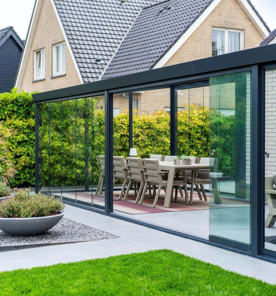 Beautiful glass Veranda Garden room in black finish, with bright white slabs and a light brown dining table and chairs inside. Grass to front lawn.