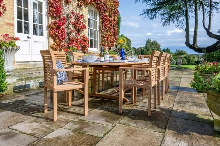 Teak Wooden outdoor dining set on a stone patio with a house and garden in the background