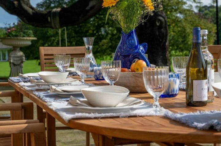 teak Dining table set for a meal outdoors with wine, glasses, and a vase.