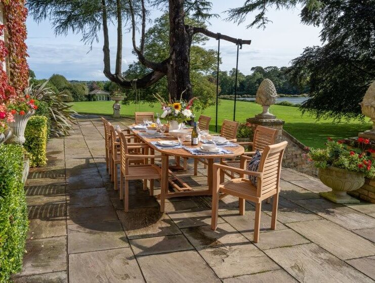 Teak Outdoor dining setup with wooden furniture and table in a garden setting.
