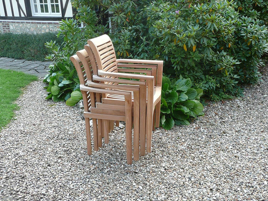 Stack of teak wooden chairs on a gravel path with greenery in the background