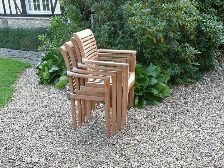 Stack of teak wooden chairs on a gravel path with greenery in the background