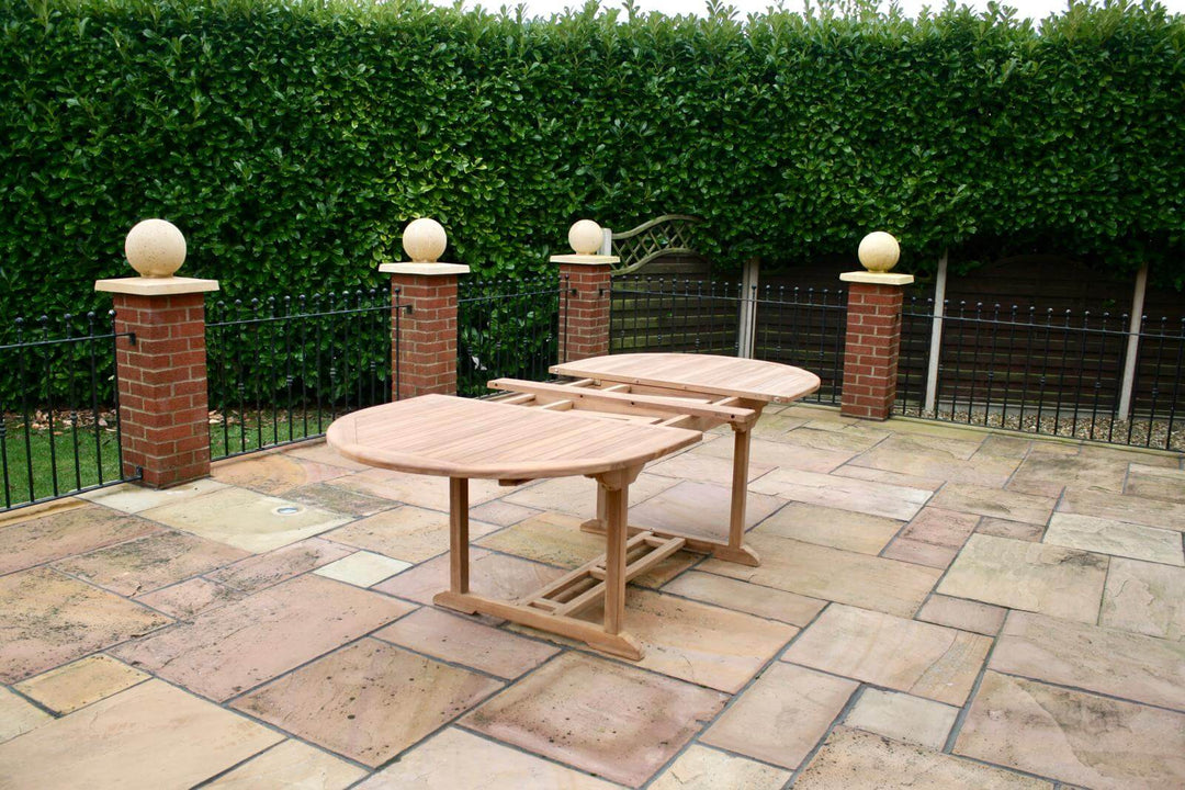 Hanover Teak Wooden outdoor dining table set on a stone patio with a hedge in the background