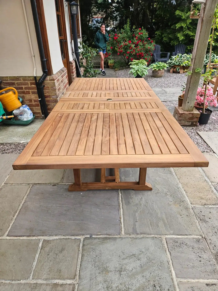 Hanover Teak Wooden outdoor dining table on a stone patio with a person and garden in the background