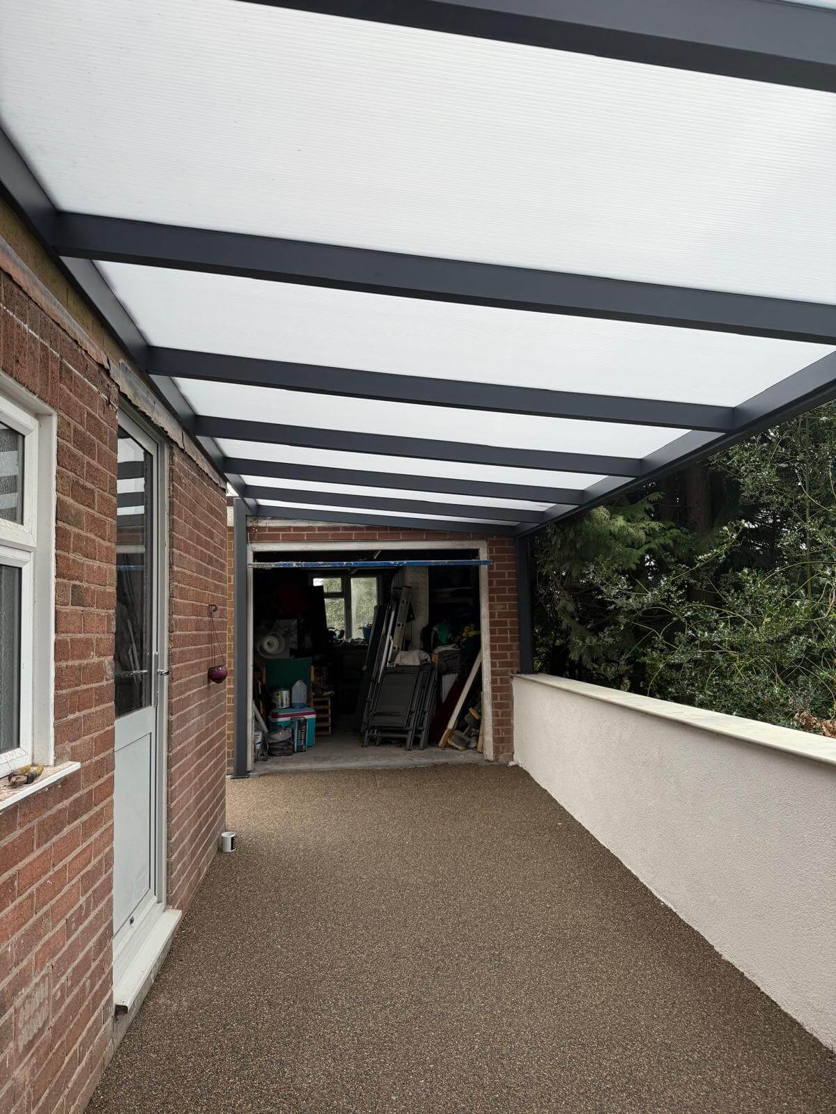 Covered outdoor area with a polycarbonate opal frosted roof providing a carport against a house in Telford Shropshire. The installation was completed by midland garden furniture.