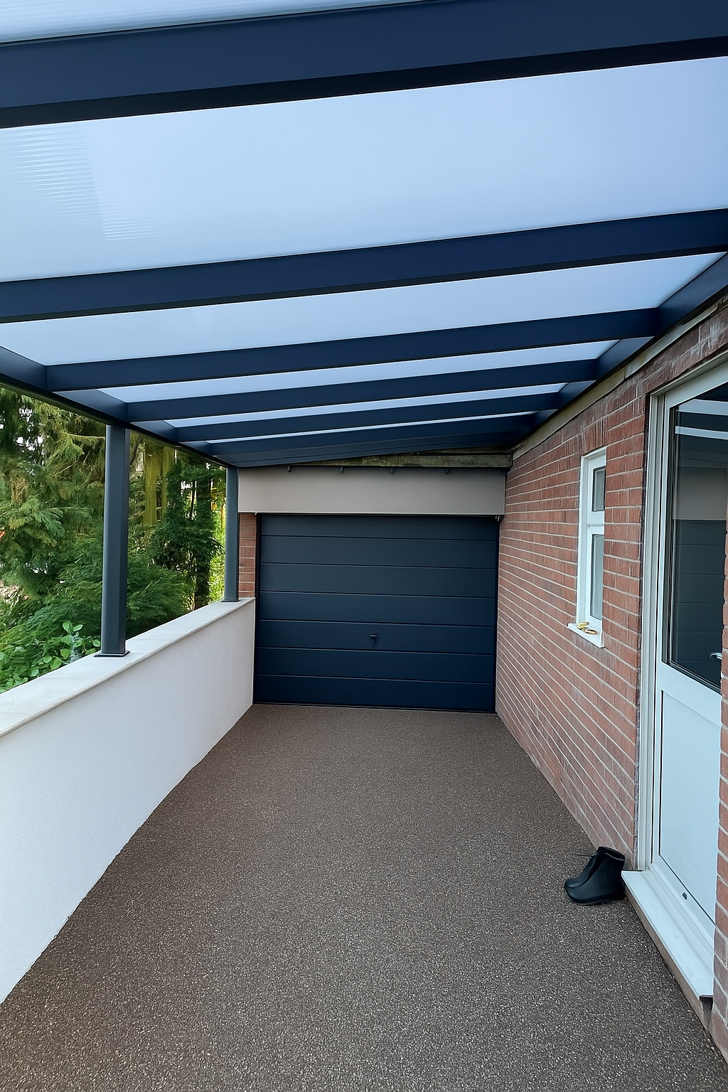 A modern Deponti carport installed by Midland Garden Furniture, featuring a sleek anthracite metal frame with a translucent opal white roof. The structure is positioned on a 1M high wall next to a resin surface drive way, with a anthracite garage door visible at the far end.