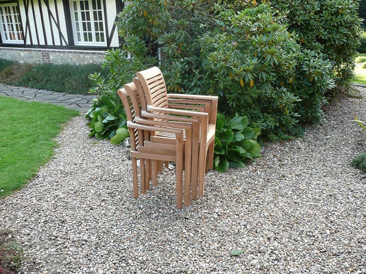 Stack of teak wooden chairs on a gravel path with greenery and a house in the background