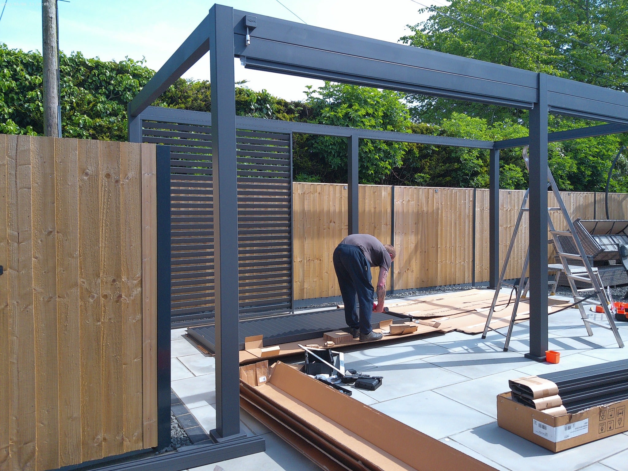 6M x 3M Grey Nova Titan Pergola under construction, on clean new light grey tiles. Midland Garden installer with power tools.