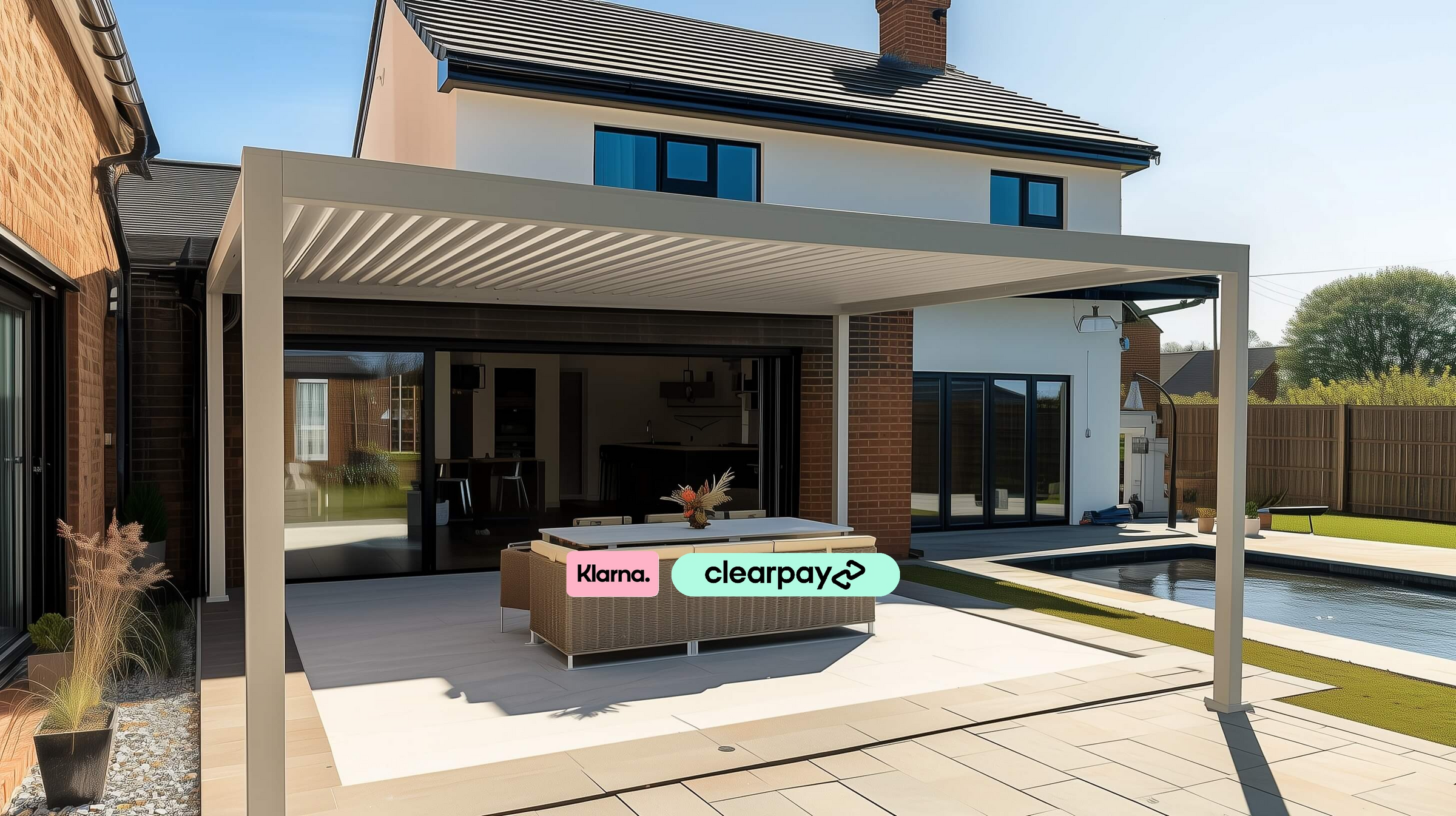 A modern back garden with pond, with a Nova Titan Pebble Grey Pergola with a modern garden sofa, table and chairs underneath.