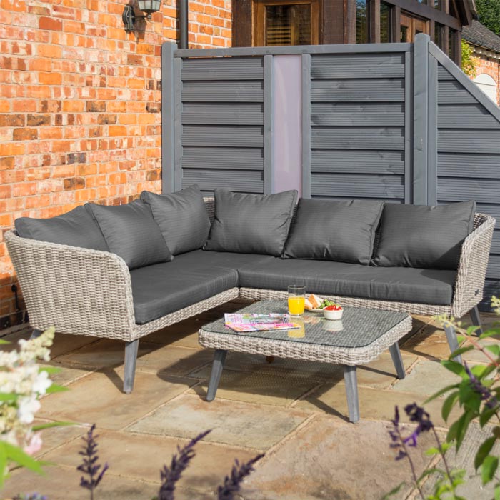 Midland Garden Furniture Heritage Collection Offley Garden furniture set, grey rattan and grey wooden legs on a sand stone patio. Corner Sofa image with coffee table with glass top.
