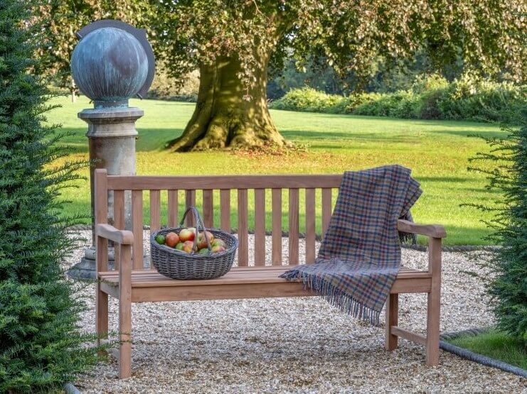 Hanover Teak Wooden bench with a plaid blanket and fruit basket in a garden setting