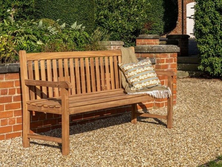 Hanover Teak Wooden bench with a cushion in a garden setting