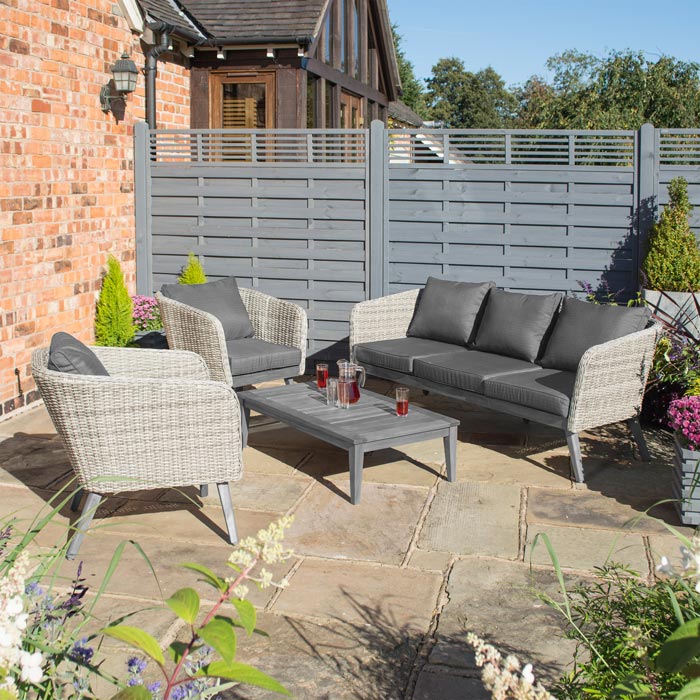 Midland Garden Furniture Heritage Collection Offley Garden furniture set, grey rattan and grey wooden legs on a sand stone patio. Image of 3 seat sofa, 2 chairs and grey coffee table.