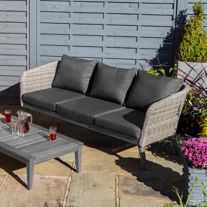 Midland Garden Furniture Heritage Collection Offley Garden furniture set, grey rattan and grey wooden legs on a sand stone patio. Close up image of the sofa with drinks on coffee table.