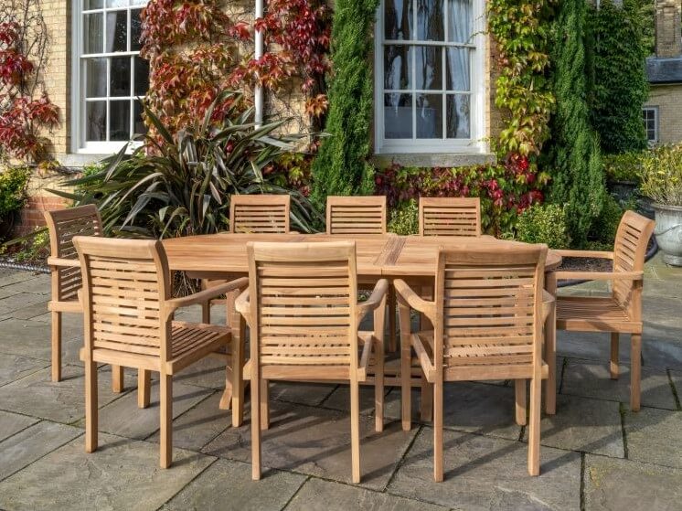 teak Wooden outdoor dining set on a stone patio with a garden and building in the background