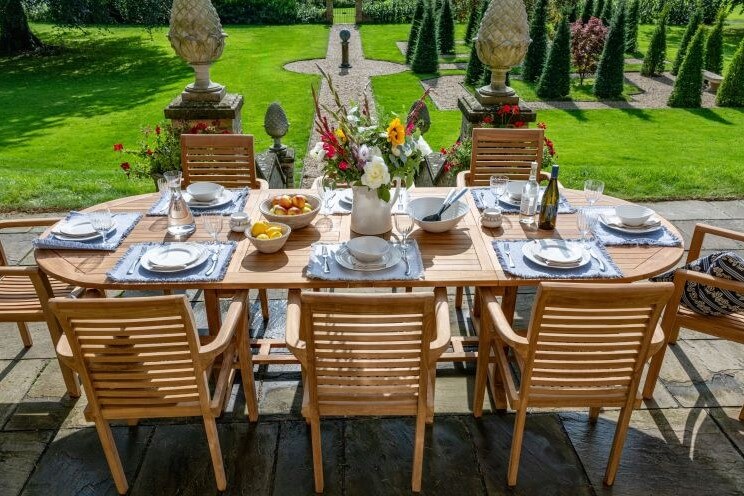 teak Dining table set for a meal outdoors with chairs and a garden view.