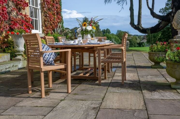 teak Outdoor patio setting with wooden dining table and chairs on a stone patio.
