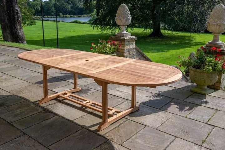 teak Wooden outdoor dining table on a stone patio with garden and trees in the background