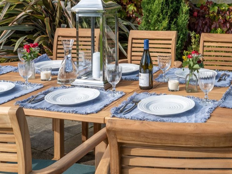 Teak outdoor Dining table set for a meal with chairs, plates, glasses, and a bottle on a patio.