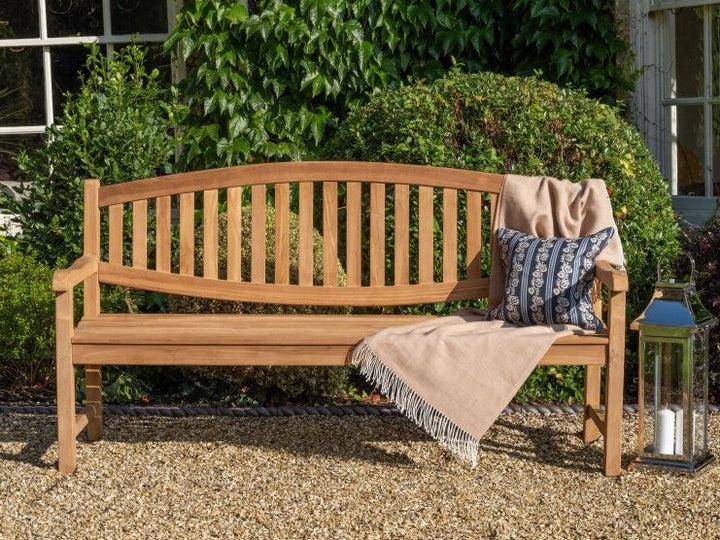 Hanover Teak  Wooden bench with a blanket and pillow in a garden setting