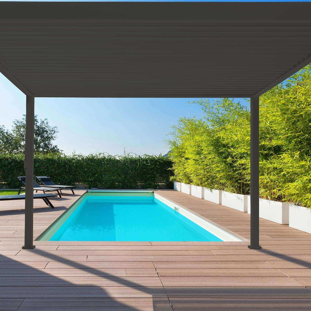 Nova Titan pergola Grey next to a Swimming pool on a sunny day. Bamboo bush to the right and sun loungers to the left, decking around the pool.