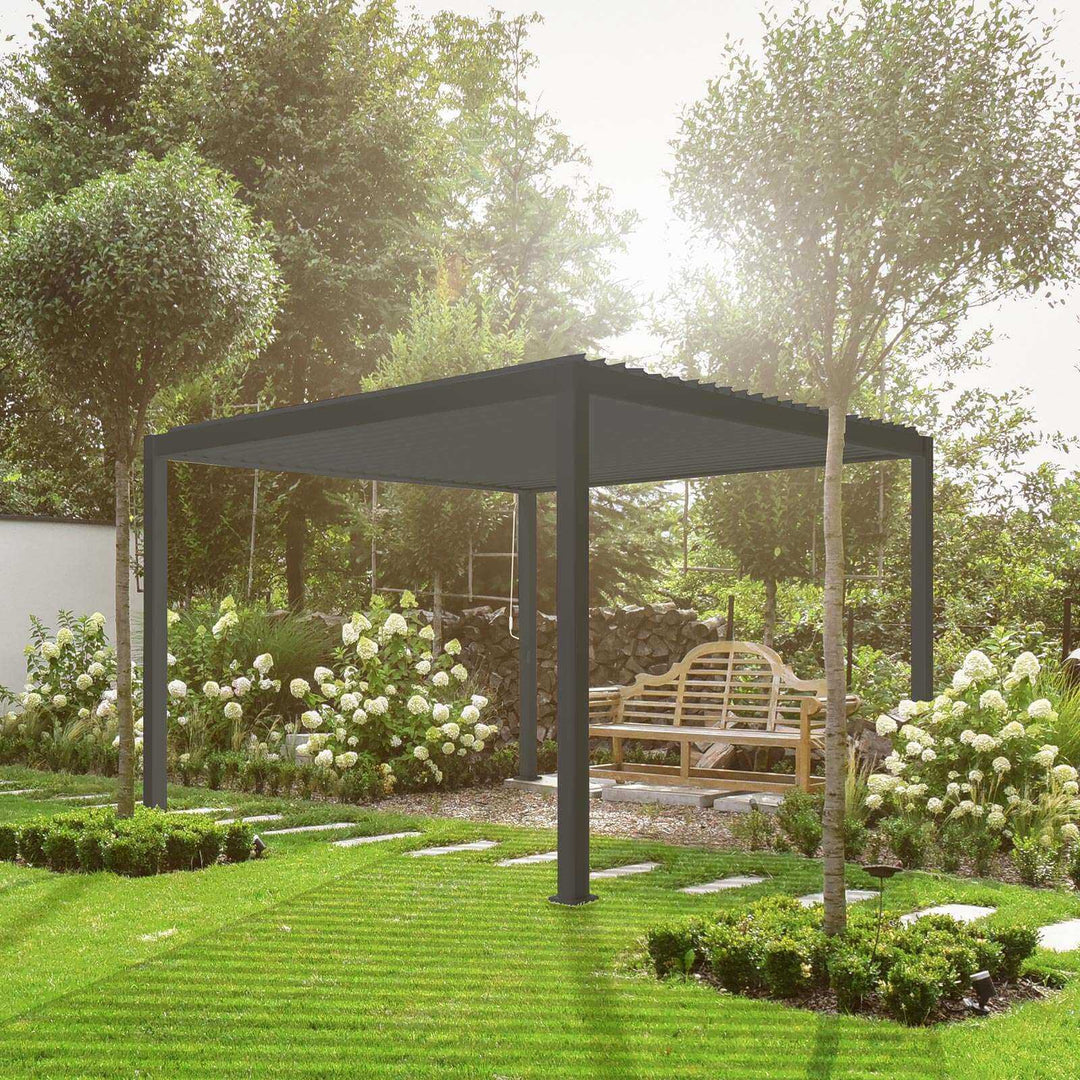 Nova Titan Pergola Grey in garden with bench underneath on a bright day. White flowers on both sides of the Pergola and tress behind