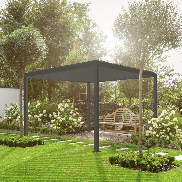 Nova Titan Pergola Grey in garden with bench underneath on a bright day. White flowers on both sides of the Pergola and tress behind
