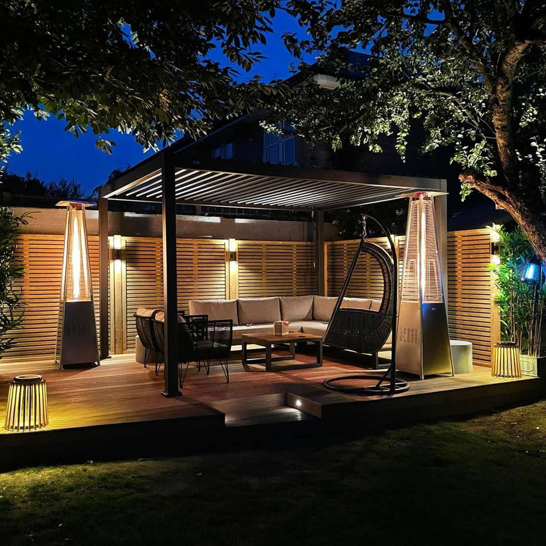 Night Time Nova Titan Pergola with wooden decking and fence behind, lit with lighting and Pergola heaters and sofa inside the Pergola.