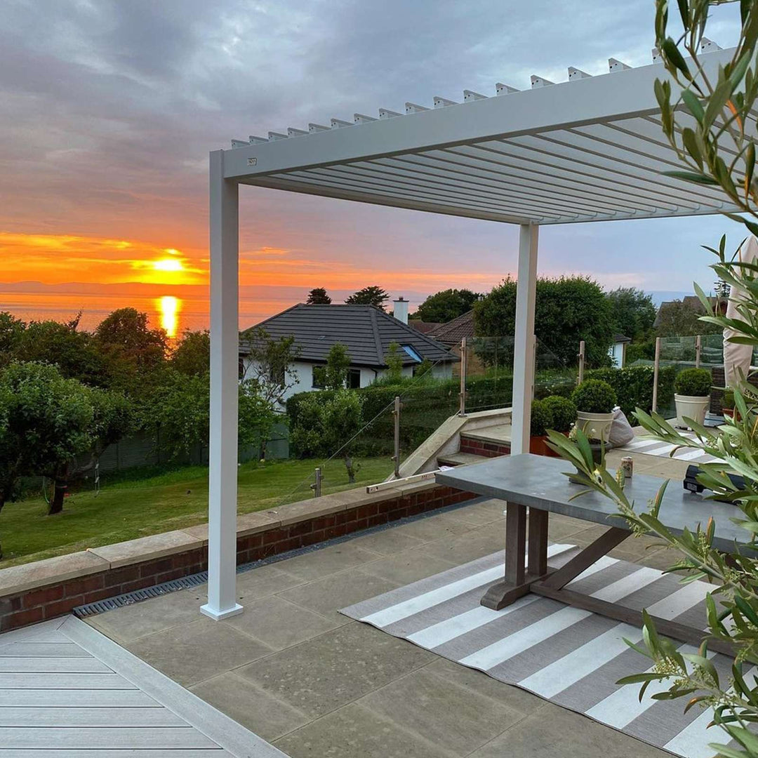 Modern Pebble Grey Nova Titan pergola on patio high up over looking a garden and the sea on the distance at dusk.