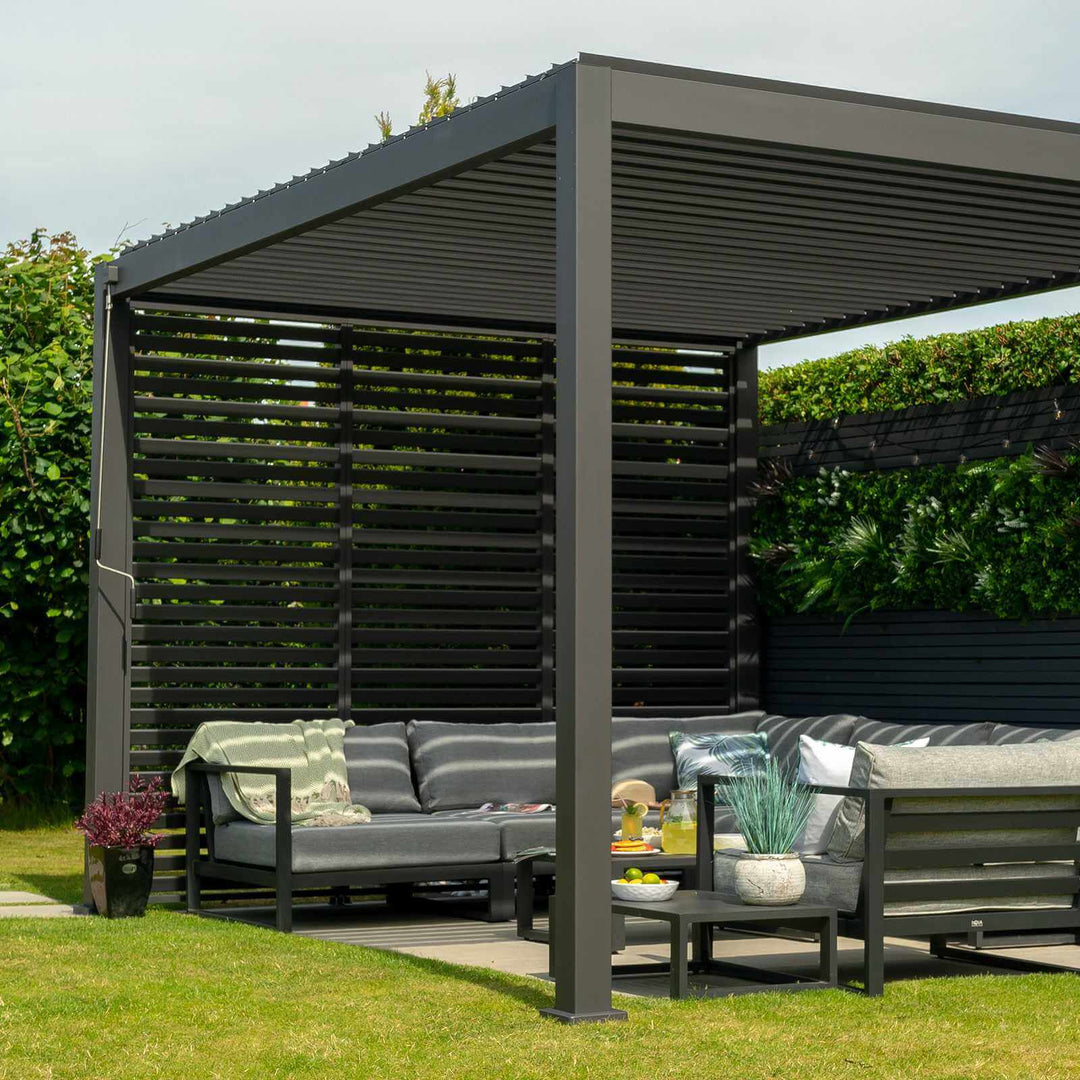 Grey Nova Titan Pergola in sunny garden with clean cut grass with louvered walls to the back and modern grey sofa set